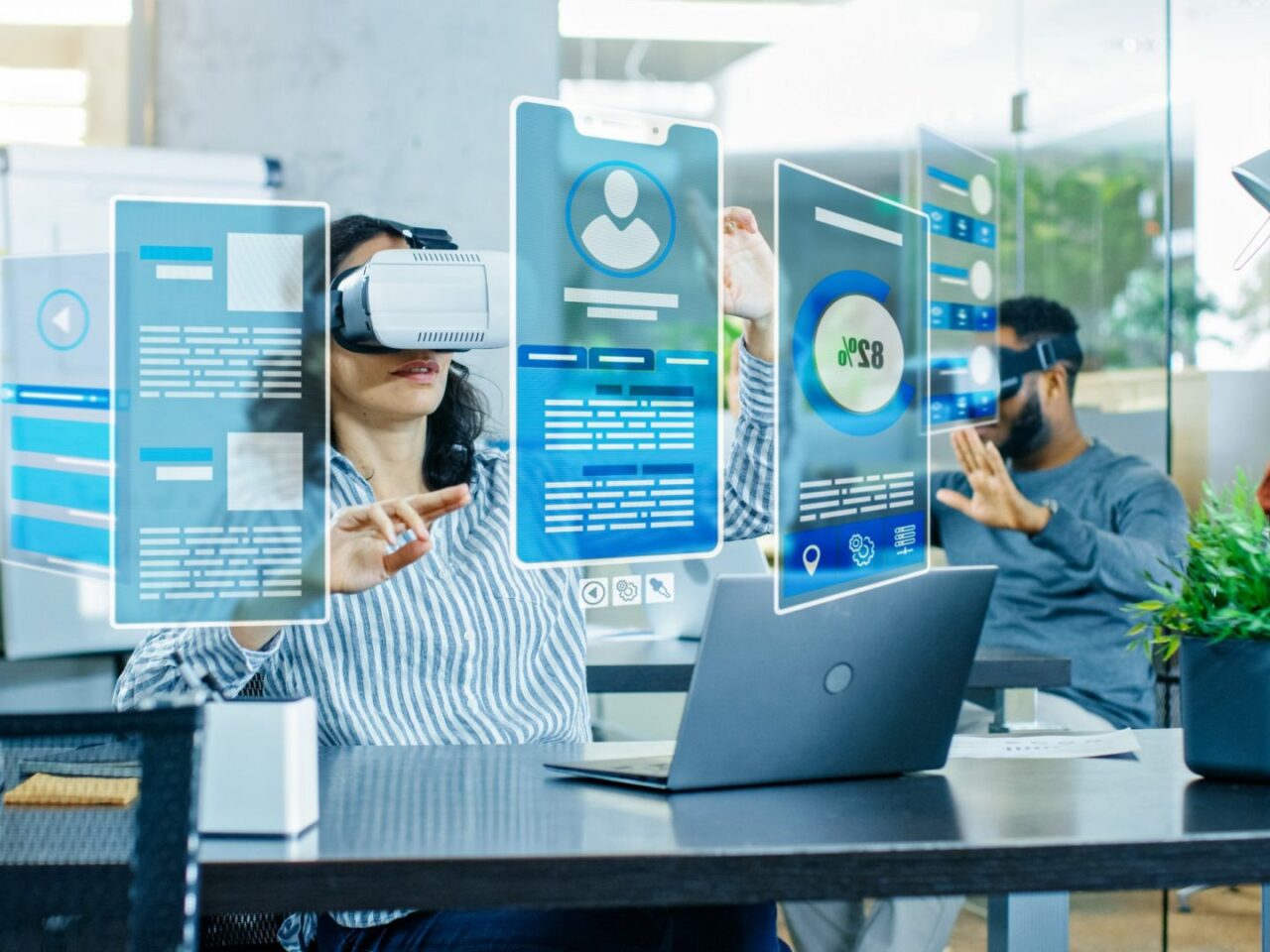 Eine weibliche Virtual-Reality-Ingenieurin/Entwicklerin trägt eine Virtual-Reality-Brille und erstellt Inhalte zusammen mit ihren Kollegen. Junge talentierte Menschen arbeiten mit Hologrammen in einem Augmented- und Mixed-Reality-Projekt.