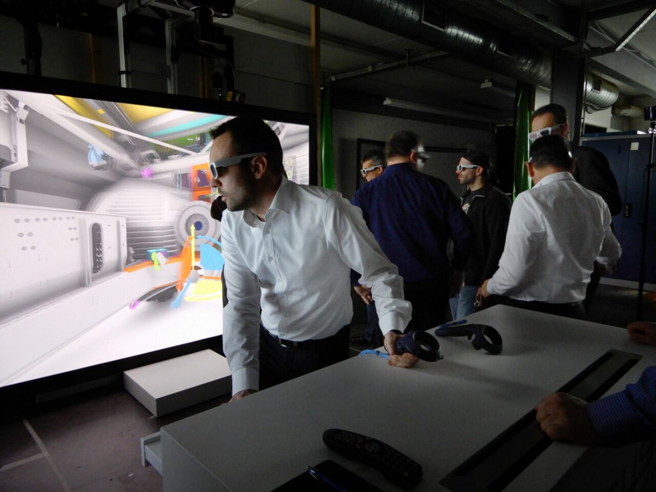 Ein Mann steht aktiv mit einer Virtual Reality-Brille vor einem Bildschirm und ist tief in die virtuelle Welt involviert. Auf dem Bildschirm ist ein Herstellungsgerät zu sehen, das aktiv etwas produziert. Die immersive Natur der VR-Brille ermöglicht es dem Mann, sich direkt mit dem Produktionsprozess der Maschine auseinanderzusetzen.