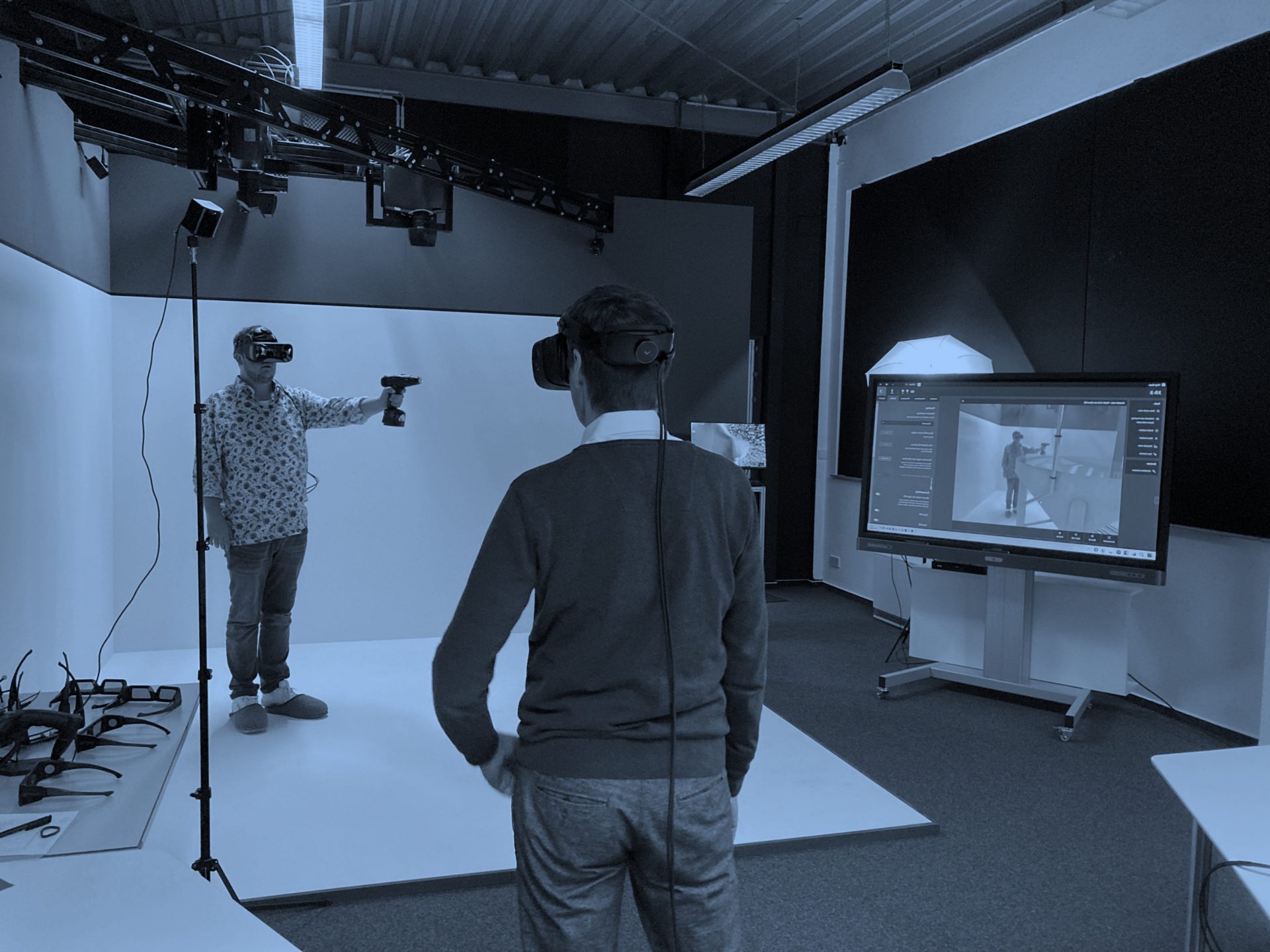 Ein Mann mit VR-Brille und Controller steht vor dem Bildschirm, auf dem seine Abbildung mit einer Maschine zu sehen ist.